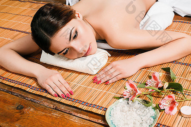 一位美丽的年轻女子在一家水疗沙龙的草席上休息。身体护理和放松的概念