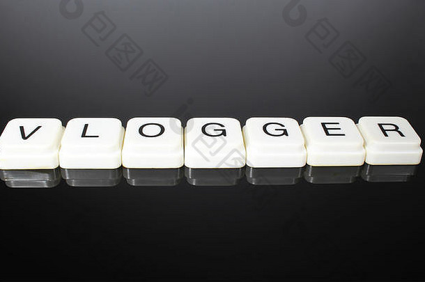 Vlogger文本单词标题标题标签封面背景。黑色反光背景上的字母玩具块。按字母顺序排列的白色字母。镜子桌上有文字的白色教育玩具块。