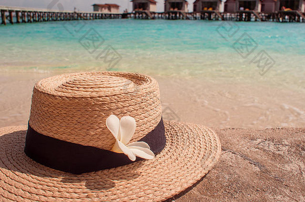 戴着帽子和棕榈叶的静物画，岛上的海滩度假。远处的水上小屋
