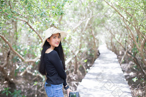 年轻的长发女孩戴着草帽，在木桥上拿着相机
