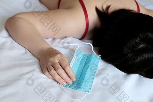 冠状病毒防护，妇女在床上睡觉时，手上拿着取下的医用口罩。COVID2019冠状病毒疾病的隔离概念