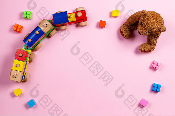 婴儿玩具背景。淡粉色背景上的泰迪熊、木制火车和彩色积木