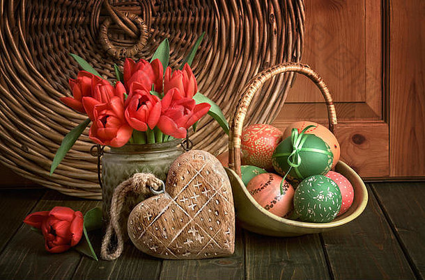 红色郁金香、木心和一篮彩色复活节彩蛋的复活节构图，深色乡村木背景