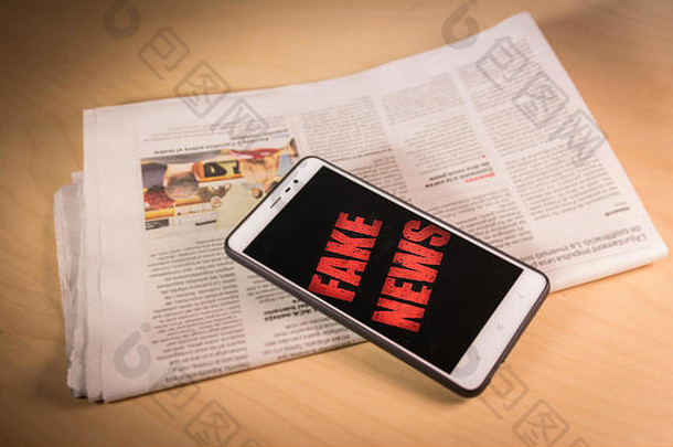 智能手机屏幕上的红色假新闻词在报纸上。骗局和假新闻概念。