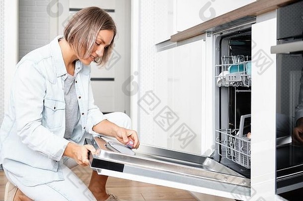 那个女人把肥皂片放进洗碗机的盒子里。带脏盘子的洗碗机。在厨房洗盘子
