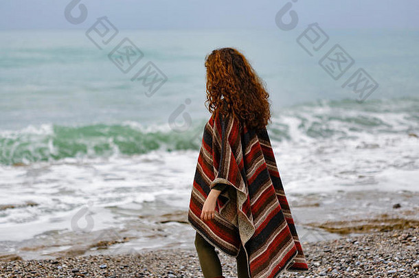 海边快乐的黑发女人的后视图肖像，穿着条纹红黑和米色斗篷