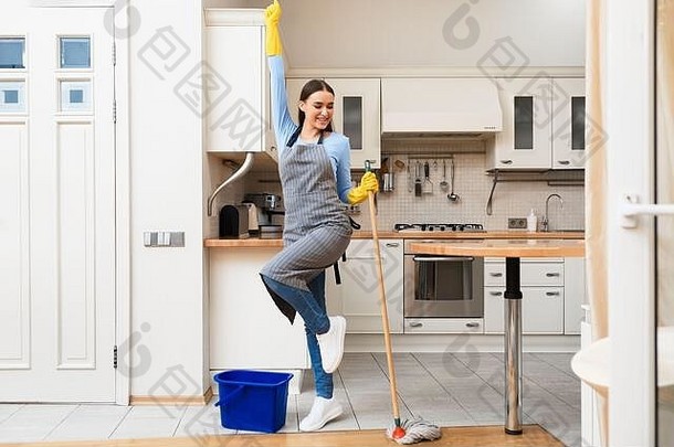 年轻的女人清洁厨房地板上跳舞拖把