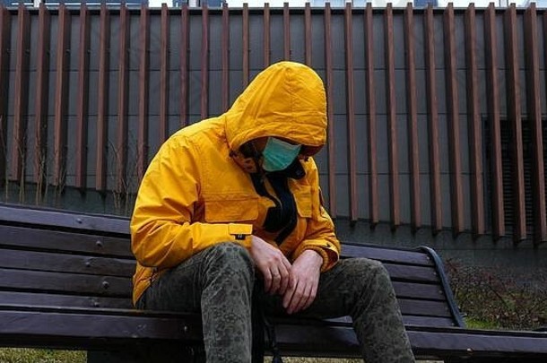 一个穿着黄色夹克和医用口罩的病人因病无力地倒在长凳上。死亡观念