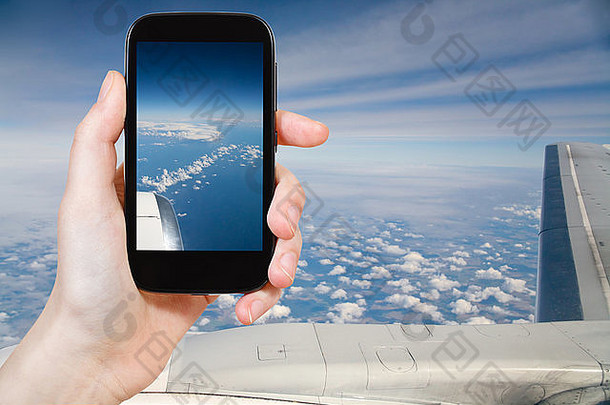 旅游理念-游客使用移动设备拍摄飞机机翼下的云层和陆地