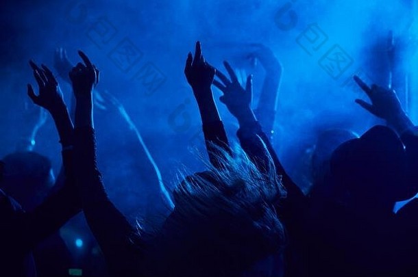 在烟雾弥漫的夜总会，年轻人一边在蓝光下观看音乐会，一边跳着、举手，空间