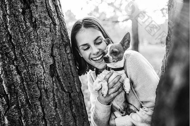 黄色秋天公园里年轻快乐的女人牵着可爱的小狗的画像