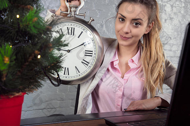 快乐的女商人手里拿着一只钟，桌上放着一棵圣诞树