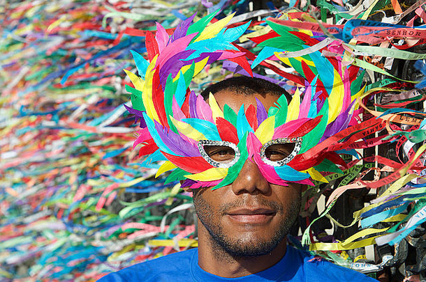 萨尔瓦多狂欢节的场景中，一名巴西男子戴着五颜六色的面具，脸上系着愿望丝带