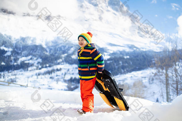 小男孩喜欢坐雪橇。儿童雪橇。蹒跚学步的孩子骑着雪橇。孩子们在户外雪中玩耍。孩子们在阿尔卑斯山滑雪