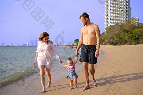 幸福的一家人在海滩上，手牵着手，挥舞着一个小女孩。妈妈爸爸女儿在海滩上散步。幸福家庭的概念。4k