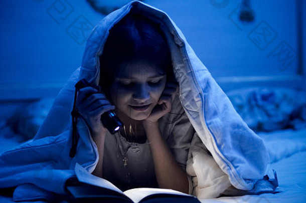 微笑的小女孩睡觉前在黑暗的卧室里看书