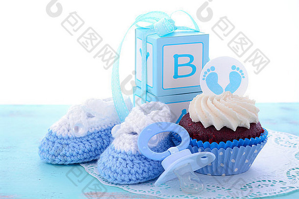 这是一个男孩蓝色的婴儿淋浴杯蛋糕，在破旧别致的蓝木桌子上有婴儿脚饰和装饰品。