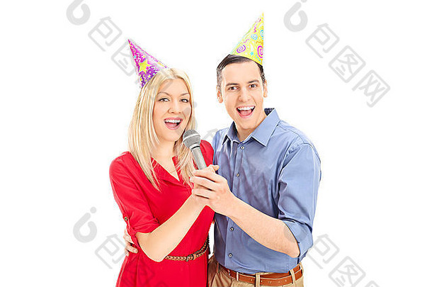 戴着派对帽的年轻夫妇在白色背景上隔着麦克风唱歌
