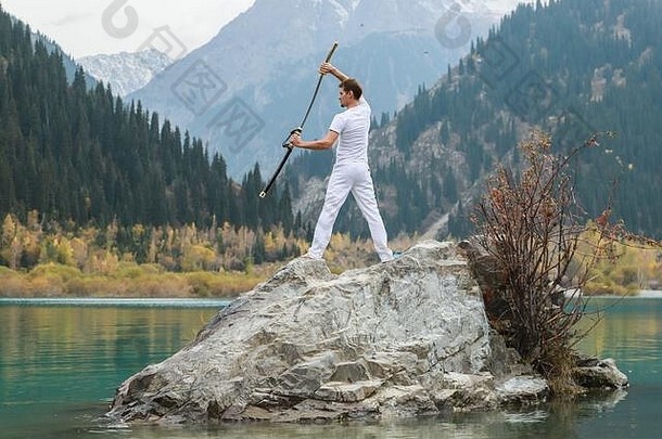 一个年轻人站在一块大石头上，手里拿着一把日本剑。