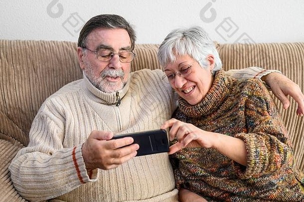 2019冠状病毒疾病。快乐的退休老夫妇，用手机打家庭视频电话。社交距离，积极的表达。