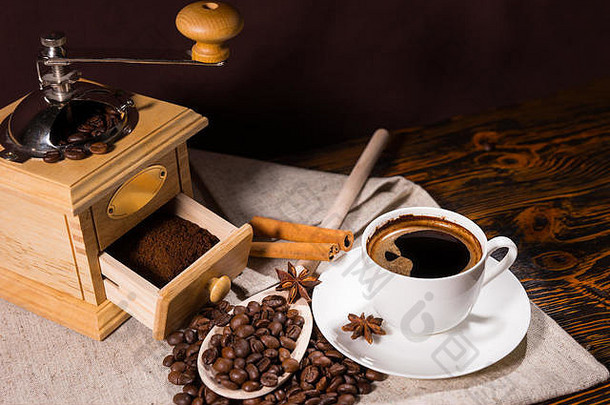研磨机，咖啡豆旁有新磨好的咖啡，白色杯子旁有木勺，上面装饰着八角茴香和肉桂棒