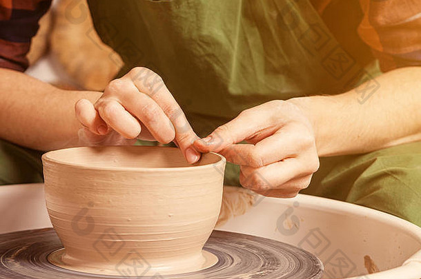 特写镜头：一位穿着格子衬衫和绿色围裙的女陶工，漂亮地雕刻了一个深碗的棕色粘土，并在一个陶工的轮子上切下多余的粘土