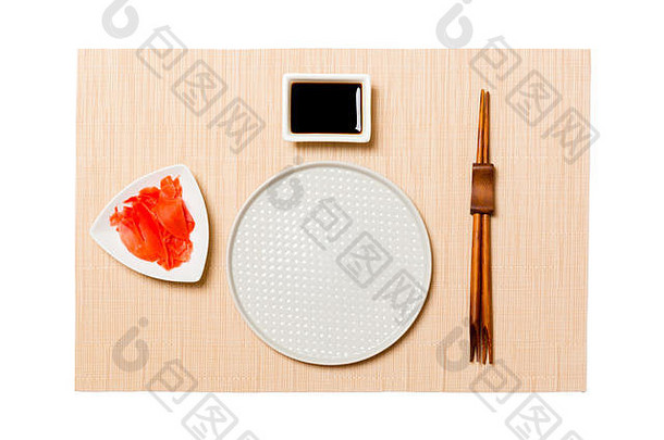 空的圆形白色盘子，用筷子在棕色寿司垫上放寿司、生姜和酱油。带有供您设计的空间的俯视图。