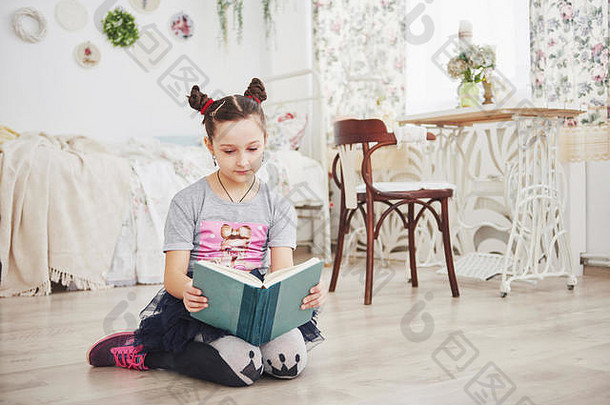 可爱的小女孩在卧室看书。戴着皇冠的孩子坐在靠窗的床上
