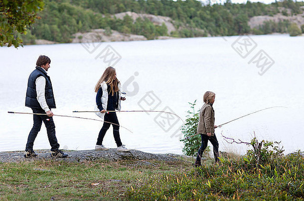 父亲带着两个孩子沿着湖岸散步
