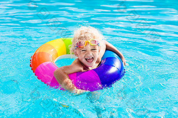 炎炎夏日，快乐的小男孩在室外游泳池里玩着五颜六色的充气戒指。孩子们学习游泳。儿童水玩具。儿童游戏