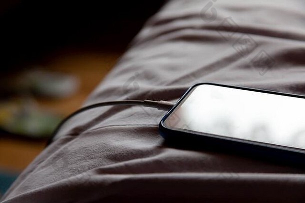 简单的现代智能手机铺设床上皱巴巴的白色表充电早....特写镜头卧室背景离开电话设备