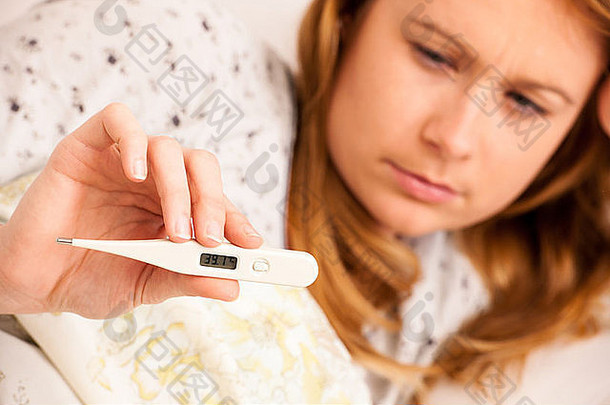 一名妇女正在用数字测温仪检查发烧，一名患流感的女孩正在床上休息