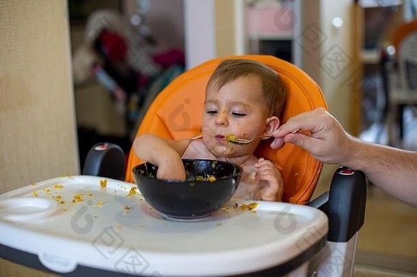 可爱的婴儿女孩橙色孩子座位吃挖掘手板勺子举行父特写镜头前面视图软