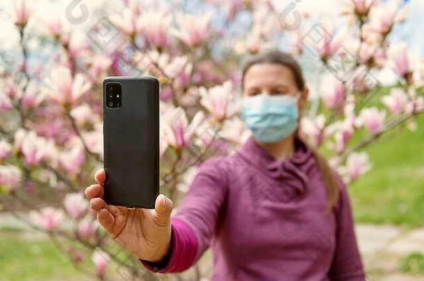 隔离期间，一名戴医用口罩的妇女在空旷的花园里与木兰花自拍