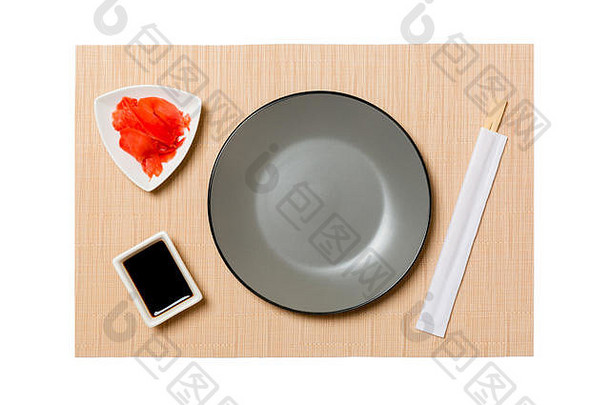 空的圆形灰色盘子，用筷子盛寿司和酱油，生姜放在棕色寿司垫上。带有供您设计的空间的俯视图。