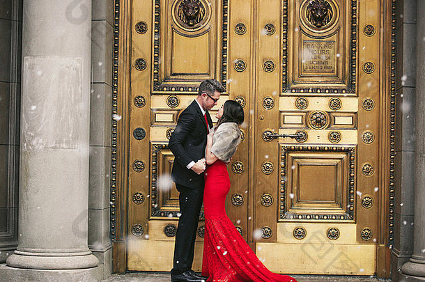 一个穿着红色长裙、鱼尾裙和毛皮的女人，一个穿着西装的男人接吻