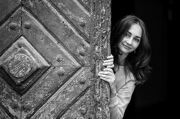 美丽的年轻女孩从古老的木门后面窥视，<strong>黑白</strong>照片。