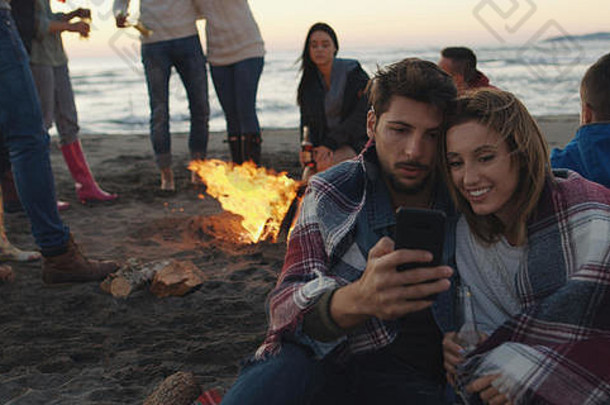 情侣们在沙滩派对上用手机和朋友们一起喝啤酒，玩得很开心