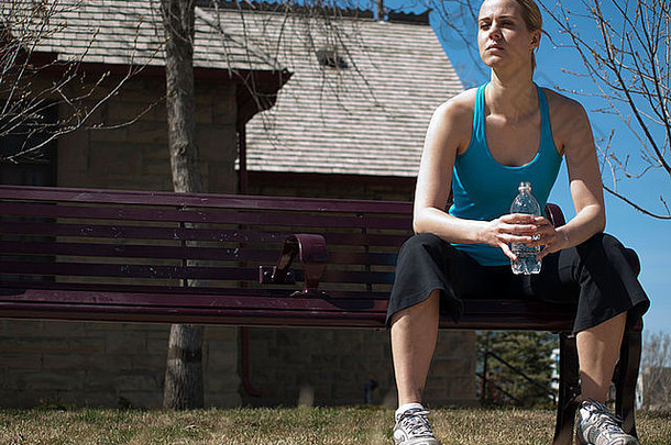 坐在长凳上拿着水瓶的年轻女子