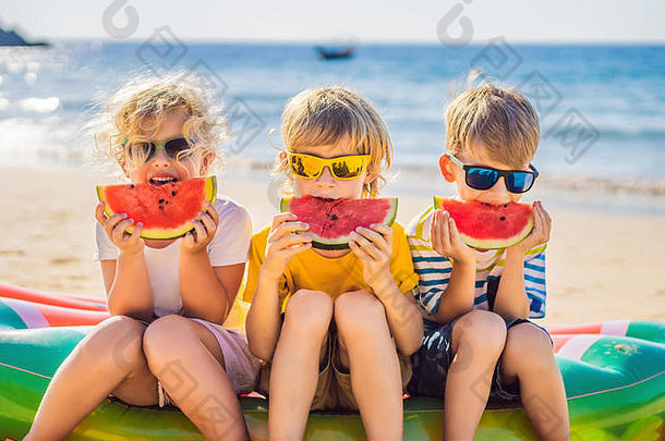 孩子们戴着墨镜在海滩上吃西瓜