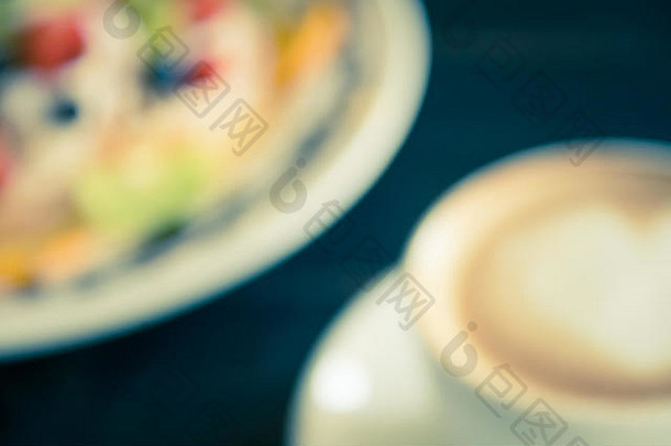 白色咖啡杯中的复古模糊心形泡沫牛奶拿铁艺术，黑木桌上有甜点。心形泡沫牛奶拿铁艺术热饮料
