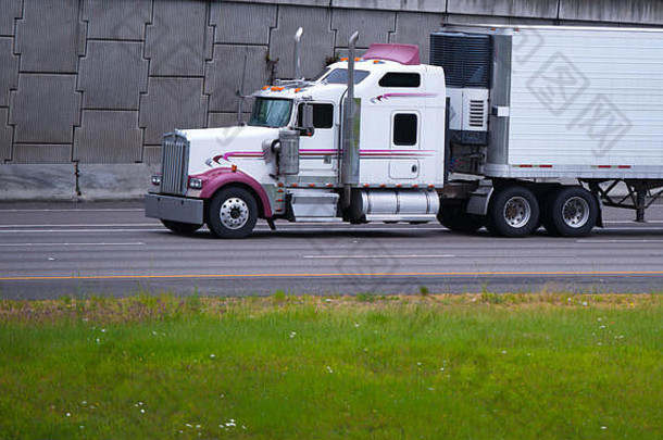 经典的大型钻机半卡车，挡泥板、扰流板和高尾管上带有彩色标志，牵引带制冷装置的拖车进行运输