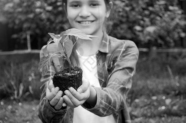 手捧嫩芽和泥土的微笑小女孩的黑白肖像
