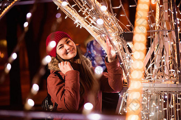 穿冬衣的女孩在灯光背景下，靠近圣诞树的灯光