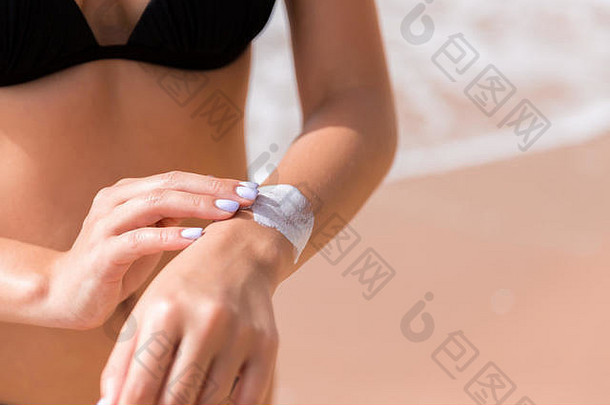 海滩上，一位皮肤黝黑的妇女正在手上涂<strong>防晒霜</strong>。