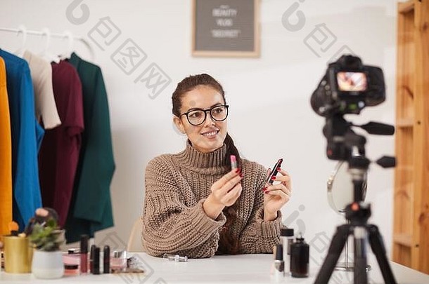 《空间》美容与生活频道拍摄视频时，微笑的年轻女子向镜头展示化妆品的肖像