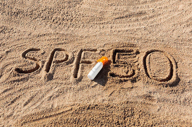 防晒系数50。SPF 50字写在沙子上，白色的瓶子上涂有防晒霜。皮肤护理概念背景。