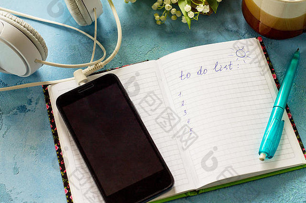 智能手机、铃兰、耳机、咖啡杯和石桌上的笔记本。
