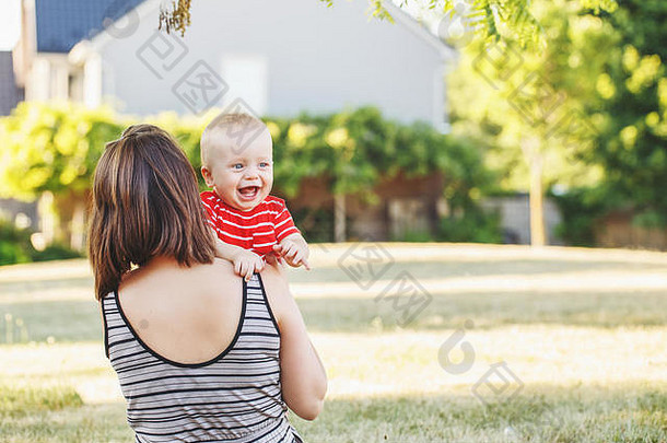 户外草地上白人母亲和穿着红色t恤的的集体肖像。母亲抱着满脸笑容的小儿子