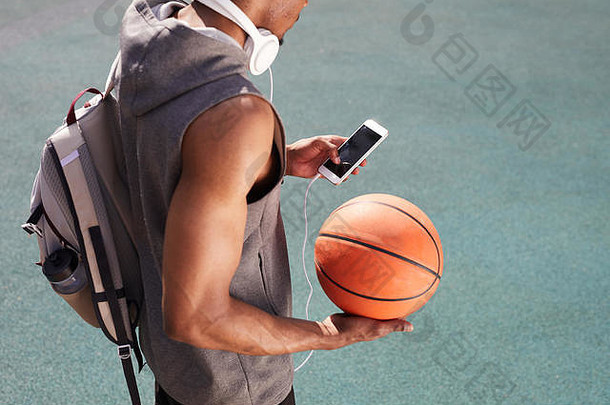<strong>无法</strong>辨认的非洲裔美国人手持篮球，在户外使用智能手机的高角度肖像，空间背景